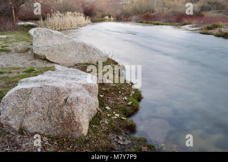 Piccolo fiume che scorre dolcemente al crepuscolo con grandi rocce sulla riva Foto Stock