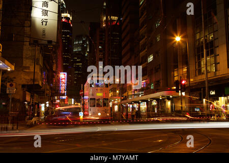 Night Shot del Vittoriano tram nel centro di Hong Kong. Striature di luce e un taxi sfocata passando davanti ad un fermo il tram. Foto Stock