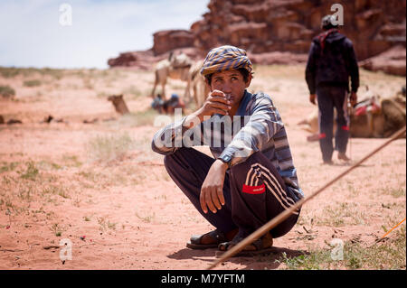 Giovane ragazzo cammello bevendo una tazza di te nel Wadi Rum desert. Foto Stock