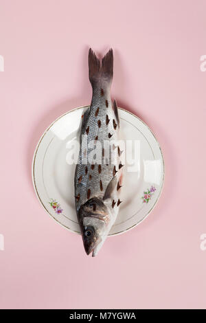 Un bass pesce con rosebush, pruni in un piatto floreale nascosto su un vivace sfondo rosa. Gioco e diversione. Colore minima ancora vita fotografia. Foto Stock