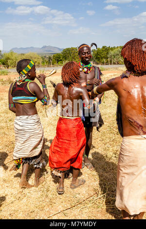 Giovani donne Hamar Taunt A Hamar Tribesman alla fustigazione essi durante un 'proveniente dall'età' Bull Jumping cerimonia, Dimeka, Valle dell'Omo, Etiopia Foto Stock