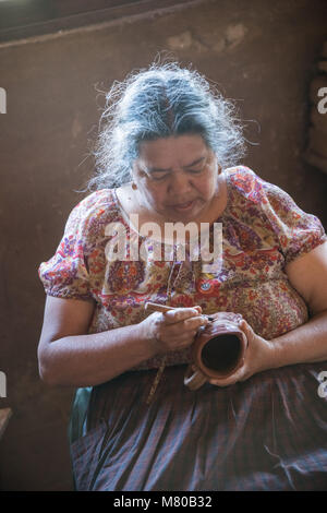 Ceramica artista Maria Fabian intaglia Purepecha tradizionali disegni in una tazza in casa loro a Santa Fe de la Laguna, Michoacan, Messico. Foto Stock