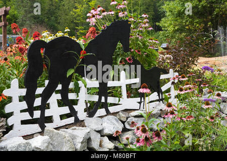 Due nero cavallo di legno ritagli contro un recinto di bianco in un terreno paesaggistico cortile anteriore giardino d'estate. Foto Stock