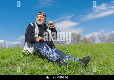 Anziani escursionista seduto su una verde collina e guardando in lontananza a stagione primavera Foto Stock