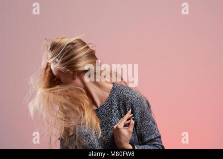 Donna con battenti capelli biondi isolato su sfondo rosa Foto Stock