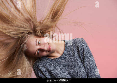 Giovane donna scuotere i capelli biondi isolato su sfondo rosa Foto Stock