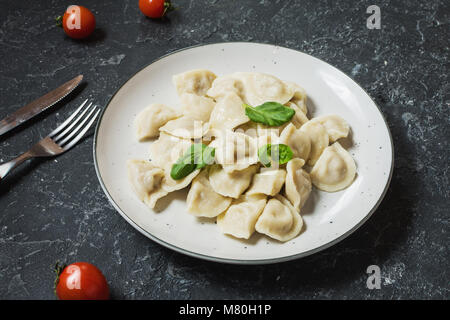 Tradizionale russo pelmeni, Ravioli, Gnocchi con carne di colore nero su sfondo di calcestruzzo. Foto Stock