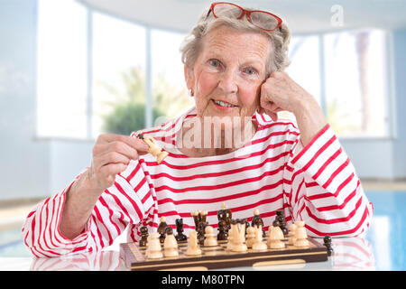 Senior vecchia donna giocando a scacchi, il movimento dei pezzi attraverso la scacchiera su grande sfondo di vetro Foto Stock