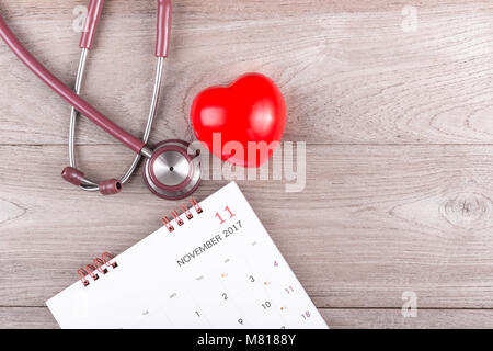 Controllare il concetto di cuore : cuore rosso, calendario e stetoscopio marrone sul tavolo di legno dello sfondo. Vista superiore Foto Stock