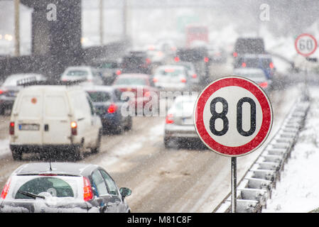 In inverno il traffico durante la tempesta di neve con scarsa visibilità. Segnale di limite di velocità con un traffico in background su una strada sdrucciolevole coperto con sn Foto Stock