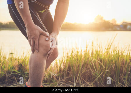 Pregiudizio dal concetto di allenamento : l'uomo asiatico di usare le mani tenere sul suo ginocchio durante il funzionamento su strada nel parco. Girato in mattinata il tempo, la luce del sole e caldo effe Foto Stock