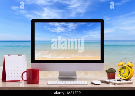 Moderno computer desktop, tazza di caffè, Sveglia, notebook e calendario sul tavolo di legno e la vista della spiaggia tropicale sfondo. Salvate con il ritaglio di pat Foto Stock