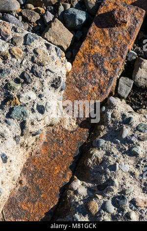 Di ferro arrugginito bar impregnato roccioso tra i blocchi di calcestruzzo con un bullone visibile Foto Stock