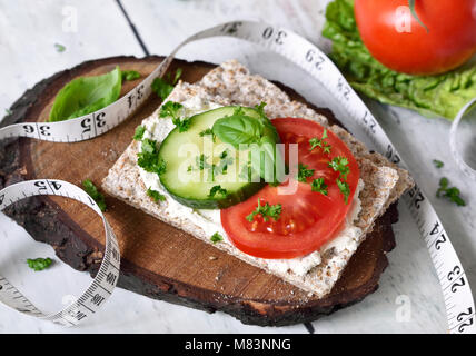 Mangiare sano o diete scena con pane croccante e di pomodori freschi e di cetriolo. Metro a nastro e un tavolo di legno. Foto Stock