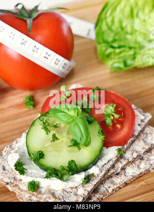 Mangiare sano o diete scena con pane croccante e di pomodori freschi e di cetriolo. Metro a nastro e un tavolo di legno. Foto Stock