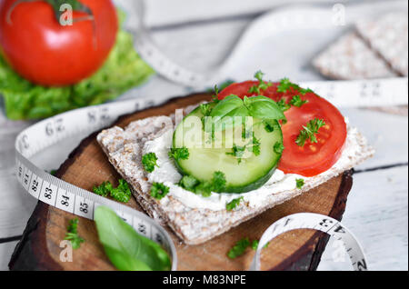 Mangiare sano o diete scena con pane croccante e di pomodori freschi e di cetriolo. Metro a nastro e un tavolo di legno. Foto Stock