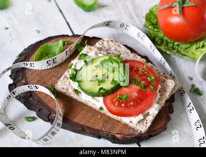 Mangiare sano o diete scena con pane croccante e di pomodori freschi e di cetriolo. Metro a nastro e un tavolo di legno. Foto Stock