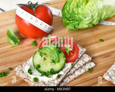 Mangiare sano o diete scena con pane croccante e di pomodori freschi e di cetriolo. Metro a nastro e un tavolo di legno. Foto Stock