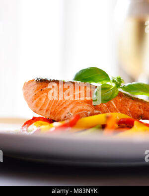 Delizioso filetto di salmone e il peperone rosso le verdure su una piastra bianca. Pasto sano, decorato con foglie di basilico. Il cibo gourmet scena. Foto Stock