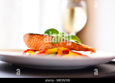 Delizioso filetto di salmone e il peperone rosso le verdure su una piastra bianca. Pasto sano, decorato con foglie di basilico. Il cibo gourmet scena. Foto Stock