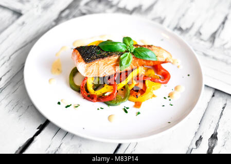 Delizioso filetto di salmone e il peperone rosso le verdure su una piastra bianca. Pasto sano, decorato con foglie di basilico. Grigliata di filetto di salmone. Foto Stock