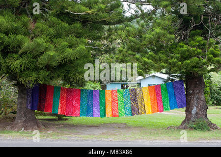 I colori dell'arcobaleno, vivacemente colorato materiale appesi ad asciugare tra due alberi a Cook Island South Pacific. Foto Stock