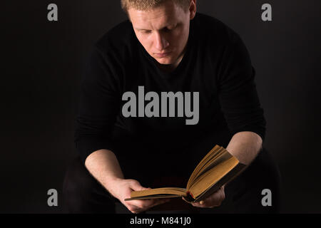 L'uomo la lettura da soli il libro al buio a illuminazione debole Foto Stock