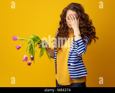 Ha sottolineato la donna elegante in camicia a righe contro sfondo giallo con fiori appassito Foto Stock