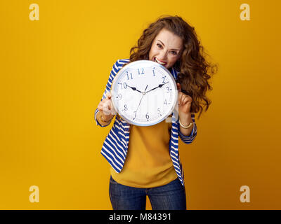 Ha sottolineato la donna elegante con lunga ondulato brunette capelli contro sfondo giallo orologio pungente Foto Stock