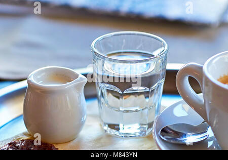 Una tazza di caffè con un rametto di acqua e latte su un vassoio con un biscotto Foto Stock