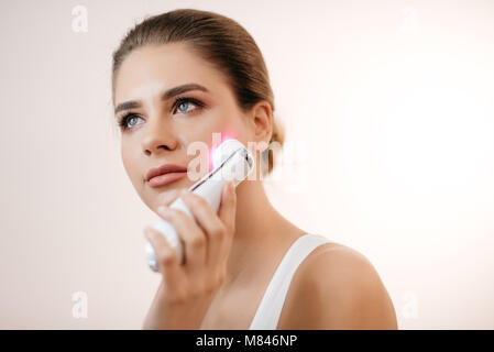 I giovani sani e freschi donna con naturale per il make-up utilizzando il viso elettrico massaggiatore a isolato sullo sfondo bianco. Foto Stock