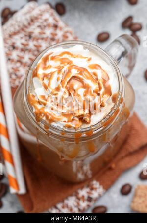 Caffè ghiacciato in latte in un Mason jar con sciroppo di caramello e panna montata. Messa a fuoco selettiva Foto Stock