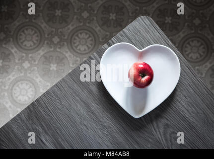 Guardando verso il basso a partire da sopra su una tabella con un cuore piastra sagomata e un colorato di rosso Apple in grigio nei dintorni. Foto Stock