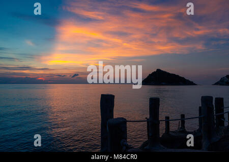 Incredibile tramonto sul mare, affacciato su Isola Nang Yuan da Ko Tao, bastoni di legno di un molo in primo piano e una rosa giallo arancio e blu cielo Foto Stock