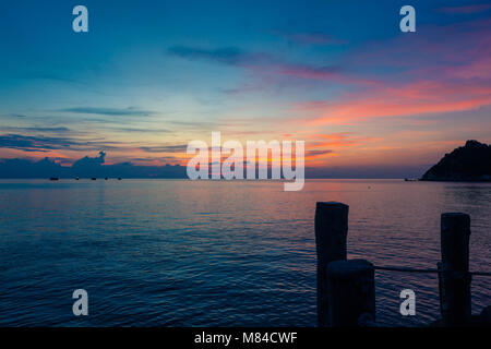 Incredibile tramonto sul mare, affacciato su Isola Nang Yuan da Ko Tao, bastoni di legno di un molo in primo piano e una rosa giallo arancio e blu cielo Foto Stock