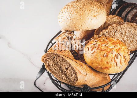 Varietà di freschi fatti in casa pane di grano in un cestello di metallo, il marmo bianco di sfondo spazio di copia Foto Stock