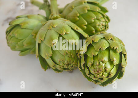 Quattro di carciofi crudi su una tavola di marmo Foto Stock