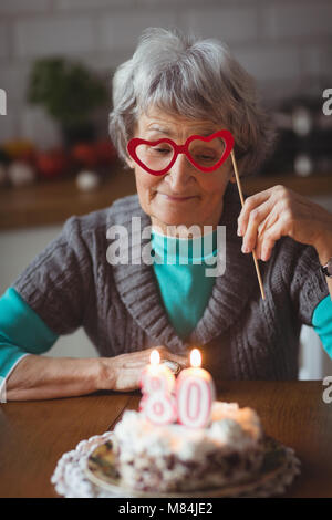 Senior donna con torta di compleanno holding masquerade mask Foto Stock