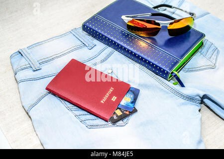 Red Passaporto russo con carte di credito, bicchieri e notepad giacciono su jeans. Il concetto di viaggio Foto Stock