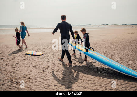 Vista posteriore del colpo di una famiglia a camminare verso il mare per fare surf. Foto Stock