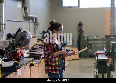 Falegname femmina utilizzando una macchina su un pezzo di legno Foto Stock