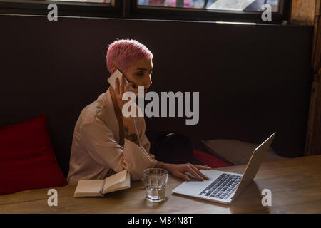 Donna elegante utilizzando computer portatile mentre l uomo parlando al telefono cellulare presso il ristorante Foto Stock