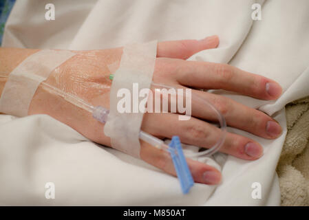 L'immagine orizzontale di mano con fluido intravenious nastrato poggiante su coltre bianca in ospedale. Terapia intravenosa Foto Stock