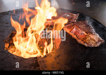 Bistecche deliziose su una artigianale di griglia per il barbecue con le fiammelle innalzantisi dal carbone al di sotto Foto Stock