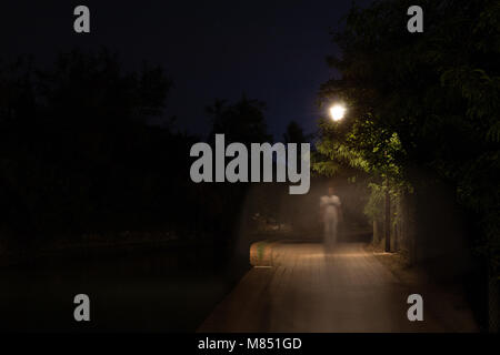 La doppia esposizione scena notturna di persona a piedi via scuro illuminato con lampioni. La sfuggente silhouette maschio sulla strada nel parco. Essere umano Foto Stock