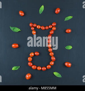 Il cibo italiano modello di mangiare con la lettera 'I' composta da molti rossi pomodori ciliegia e le foglie di basilico isolato su sfondo blackboard Foto Stock