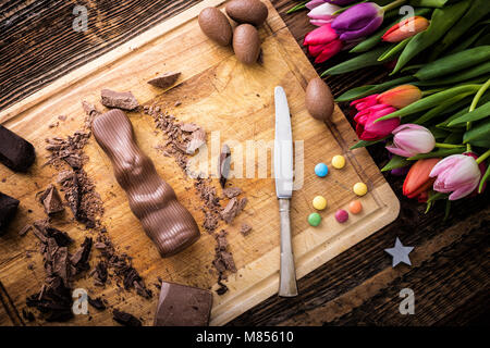 Il coniglio di cioccolato e pezzi grezzi di cioccolato con confetto e tulipani. Foto Stock