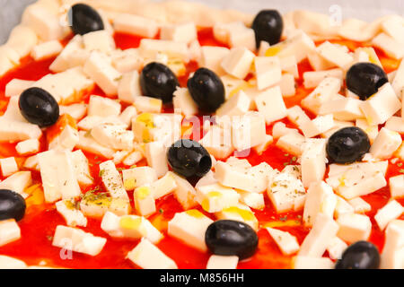 Pizza cruda decorate mozzarella, olive nere e salsa di pomodoro pronto per essere cotto al forno Foto Stock