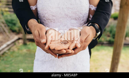 Close up della sposa e lo sposo mettere le mani insieme e tenere gli anelli di nozze sulla loro palmi. In prossimità dei due anelli di nozze il recente colpo di stato sposato Foto Stock