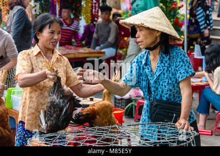 Un cliente risate con una donna che indossa un tradizionale vietnamita di bambù conica hat come lei si mantiene un chcken dalle gambe in Hoi An, Vietnam Foto Stock